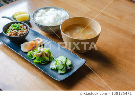A Japanese breakfast set with natto (fermented soybeans). Rice, miso soup, a small bowl, and side dishes are arranged on a wooden table. A Japanese breakfast set with natto (fermented soybeans). Rice, miso soup, a small bowl, and side dishes are arranged on a wooden table. 138125471
