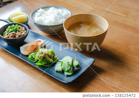 日式早餐套餐，擺放在木桌上：米飯、味噌湯、納豆（發酵大豆）、醃菜和各種小菜，盛放在長盤中。 138125472