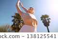 Woman in pink top and white shorts exercising beneath palm trees 138125541