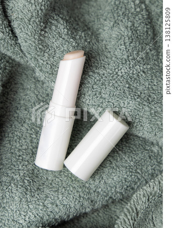 White opened lip balm stick mockup with a lid on sage green bath towel, unbranded packaging 138125809