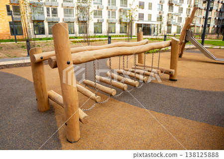 Modern wooden rope bridge on a children's playground. Outdoor entertainment and childhood adventure concept. Safe play equipment for kids. Modern wooden rope bridge on a children's playground. Outdoor entertainment and childhood adventure concept. Safe play equipment for kids. 138125888
