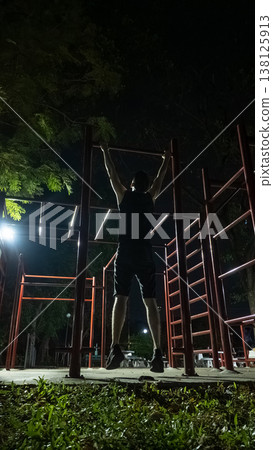 Man doing pull up exercise on outdoor bars at night urban fitness training, Male athlete performing calisthenics workout in park Man doing pull up exercise on outdoor bars at night urban fitness training, Male athlete performing calisthenics workout in park 138125913