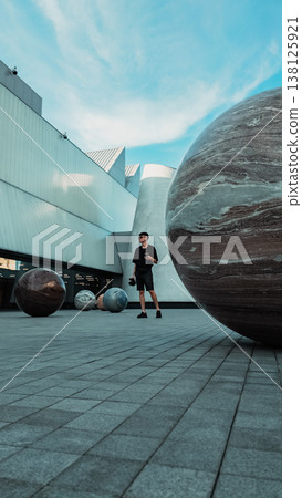 Tourist man standing by spherical stone sculptures in modern urban plaza, Male visitor exploring contemporary architecture with planet like spheres in Dib Bangkok museum Tourist man standing by spherical stone sculptures in modern urban plaza, Male visitor exploring contemporary architecture with planet like spheres in Dib Bangkok museum 138125921