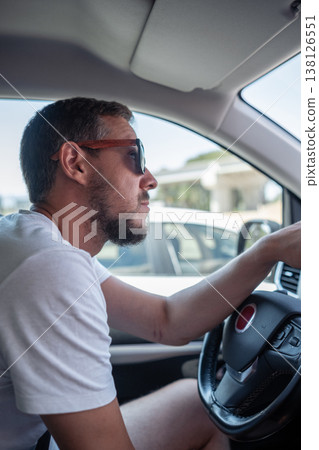 Man Driving a Car in Casual Clothing While Wearing Sunglasses on a Sunny Day in an Urban Environment Man Driving a Car in Casual Clothing While Wearing Sunglasses on a Sunny Day in an Urban Environment 138126551