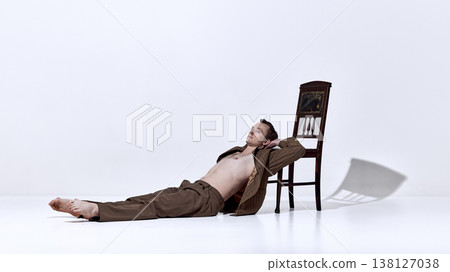 Male dancer lying on floor near chair in relaxed pose in minimal studio Male dancer lying on floor near chair in relaxed pose in minimal studio 138127038