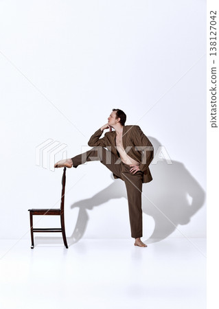 Male dancer interacting with chair in stylized pose inside minimal studio. 138127042