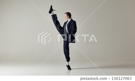 Businessman performing high kick while balancing in formal suit on neutral background. Businessman performing high kick while balancing in formal suit on neutral background. 138127063