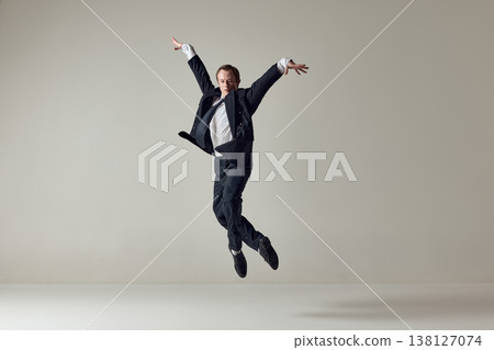 Businessman jumping with raised arms in dynamic motion on neutral background Businessman jumping with raised arms in dynamic motion on neutral background 138127074