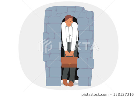 Depressed business man stands in narrow stone doorway symbolizing pressure of circumstances 138127316