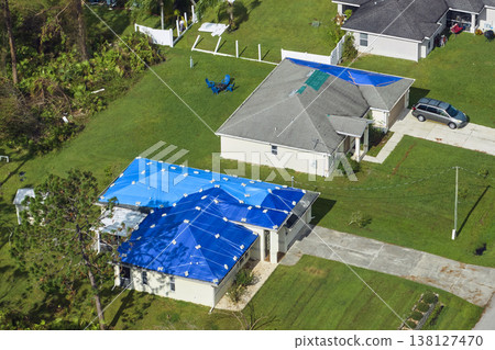 Hurricane Ian damaged house rooftops covered with protective plastic tarp against rain water leaking until replacement of asphalt shingles. Aftermath of natural disaster Hurricane Ian damaged house rooftops covered with protective plastic tarp against rain water leaking until replacement of asphalt shingles. Aftermath of natural disaster 138127470