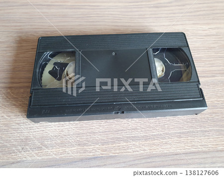 Black retro VHS video cassette lying on a wooden surface. Close-up of the back side of the analog video information carrier. 138127606