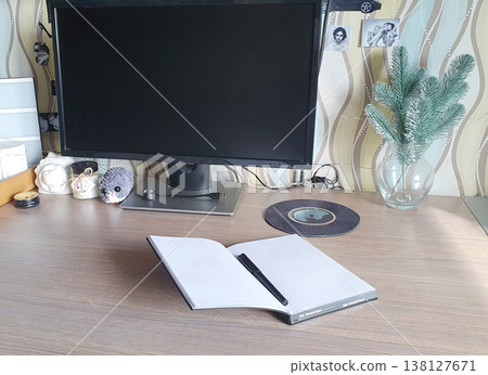 Cozy workplace at home: open notebook with pen on wooden table in front of computer monitor. Atmosphere of productivity, study and hobby. 138127671