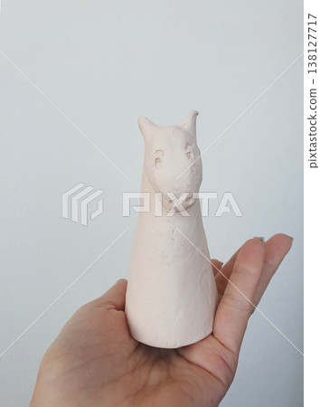 Hand holding small handmade white clay horse figurine against neutral background, minimalist craft concept. 138127717