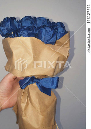 Hand holding a bouquet of blue roses made from satin ribbons wrapped in craft paper 138127751