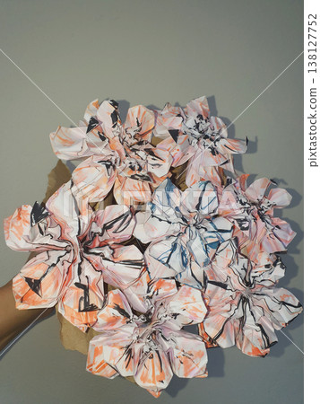 Hand holding a creative bouquet of origami paper flowers with abstract orange and black patterns 138127752