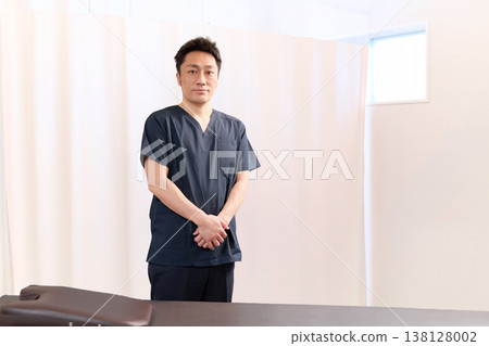 A male chiropractor standing in the treatment room of a chiropractic clinic. A male chiropractor standing in the treatment room of a chiropractic clinic. 138128002