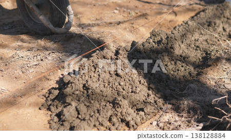 Boots Stirring Wet Cement Along Dirt Path Under Bare Branches, Shadowed Ground And Scattered Roots, Manual Effort For Rural Path Restoration, Gritty Texture And Warm Afternoon Light 138128884