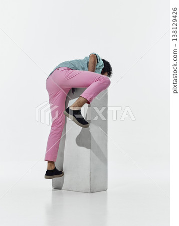 Man climbing over white pedestal in studio isolated on white background. Man climbing over white pedestal in studio isolated on white background. 138129426