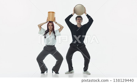 Man and woman balancing containers on head while standing in studio. Man and woman balancing containers on head while standing in studio. 138129440