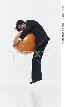 Man in formal suit leaning on large exercise ball in floating pose on white background 138129459