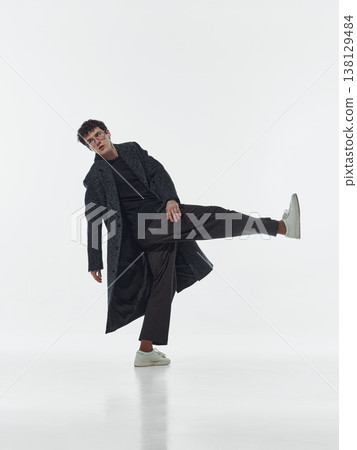 Man wearing coat losing balance with raised leg in studio isolated on white background. 138129484