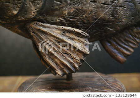 Macro shot focusing on the textured wooden fin and body of a hand-carved fish sculpture with an aged, weathered finish. Macro shot focusing on the textured wooden fin and body of a hand-carved fish sculpture with an aged, weathered finish. 138129644
