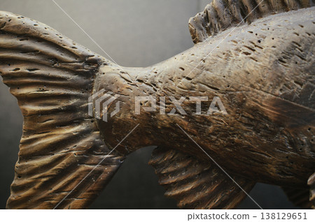 Macro shot of a hand-carved wooden fish sculpture's tail section, highlighting deep weathered textures and natural timber grain. Macro shot of a hand-carved wooden fish sculpture's tail section, highlighting deep weathered textures and natural timber grain. 138129651