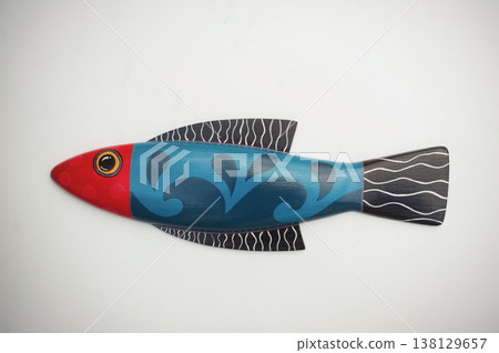Single decorative wooden fish featuring a bright red head, turquoise body with dark blue patterns, and black-and-white striped fins. Single decorative wooden fish featuring a bright red head, turquoise body with dark blue patterns, and black-and-white striped fins. 138129657