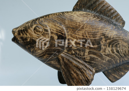 Detailed close-up of a hand-carved wooden fish sculpture, focusing on the expressive head, carved eye, and beautiful natural grain patterns of the dark timber. Detailed close-up of a hand-carved wooden fish sculpture, focusing on the expressive head, carved eye, and beautiful natural grain patterns of the dark timber. 138129674