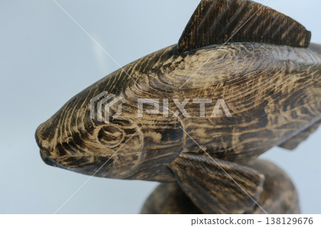High-angle macro shot of a hand-carved wooden fish head and upper body, emphasizing the detailed stylized pattern of annual rings and textural grain. 138129676