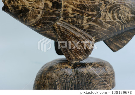 Macro shot of a hand-carved wooden fish sculpture base, emphasizing the stone-like texture of the pedestal and the detailed lower fin craftsmanship. Macro shot of a hand-carved wooden fish sculpture base, emphasizing the stone-like texture of the pedestal and the detailed lower fin craftsmanship. 138129678