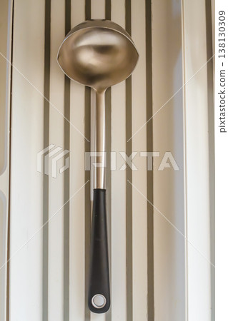 Stainless steel soup ladle with a black handle in a kitchen drawer organizer. Top view of a common kitchen utensil. 138130309