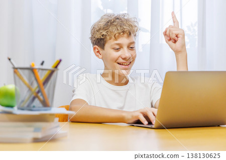 Schoolboy studying at home with laptop, notebook, and learning materials, smiling happily Schoolboy studying at home with laptop, notebook, and learning materials, smiling happily 138130625