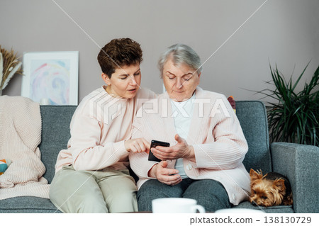 Adult woman explaining her senior mother how to use smartphone. Education for aged. Retired lady discovering mobile technology for calling, texting, buying online, playing games, using medical apps Adult woman explaining her senior mother how to use smartphone. Education for aged. Retired lady discovering mobile technology for calling, texting, buying online, playing games, using medical apps 138130729