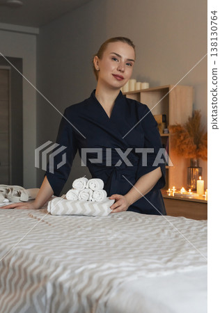 Therapist preparing massage table with fresh towels for a relaxation treatment in a serene wellness spa salon. The concept of rest, relaxation Therapist preparing massage table with fresh towels for a relaxation treatment in a serene wellness spa salon. The concept of rest, relaxation 138130764