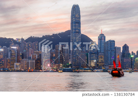 Traditional wooden junk boat with red sails against Hong Kong skyline during sunset 138130784