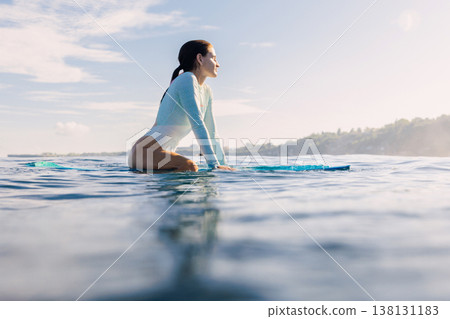 Surfer girl sitting on surfboard in ocean. Surfer woman waiting waves in Bali Surfer girl sitting on surfboard in ocean. Surfer woman waiting waves in Bali 138131183