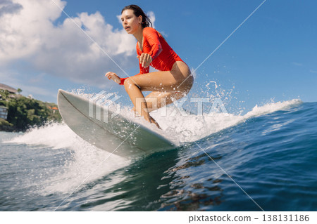 Surfer woman in swimsuit riding wave with splashes in tropical ocean Surfer woman in swimsuit riding wave with splashes in tropical ocean 138131186