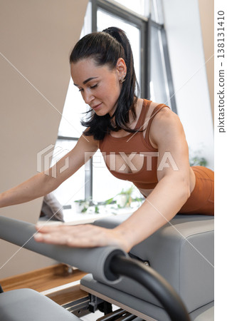 Sporty woman in orange suit practicing pilates on reformer equipment in fitness studio. Pilates practice, orange, studio, reformer, active. Sporty woman in orange suit practicing pilates on reformer equipment in fitness studio. Pilates practice, orange, studio, reformer, active. 138131410