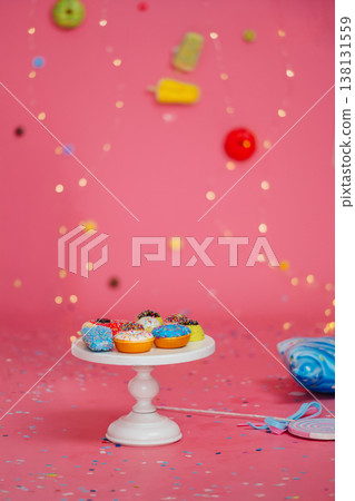 Colorful Donuts On White Pedestal, Vibrant Pink Backdrop Scattered With Candy And Confetti Colorful Donuts On White Pedestal, Vibrant Pink Backdrop Scattered With Candy And Confetti 138131559