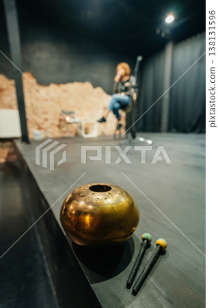 Musician Blurred On Empty Stage, Brass Bowl And Mallets In Foreground, Performer Tuning Instrument . Musician Blurred On Empty Stage, Brass Bowl And Mallets In Foreground, Performer Tuning Instrument . 138131596