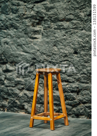 Wooden Stool Against Stone Wall, Worn Seat And Tall Legs, Workshop Or Studio Setting, Rustic Grain . 138131599