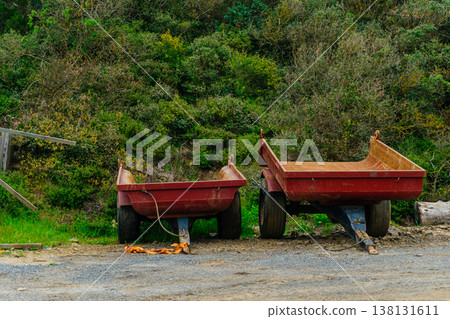 Two Weathered Red Trailers Parked Along Overgrown Roadside, Chipped Paint, Exposed Metal, Flat . Two Weathered Red Trailers Parked Along Overgrown Roadside, Chipped Paint, Exposed Metal, Flat . 138131611