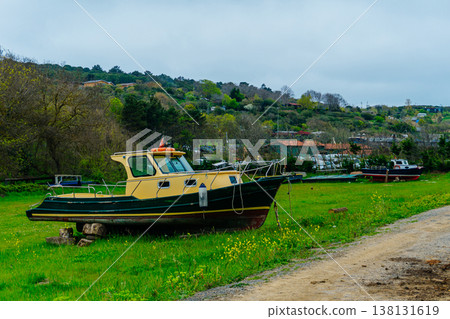 Derelict Cruiser On Grassy Riverbank, Weathered Hull With Peeling Paint And Rust, Moored Dinghies . 138131619