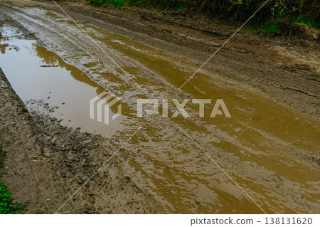 Muddy Rutted Road With Puddles Showing Deep Wheel Ruts, Slick Clay Surface And Standing Water Eroded Muddy Rutted Road With Puddles Showing Deep Wheel Ruts, Slick Clay Surface And Standing Water Eroded 138131620