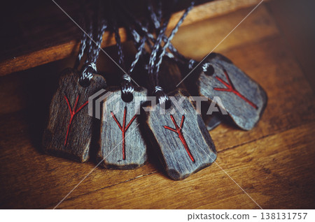 Group of four handcrafted wooden Algiz rune pendants on cords, lying on a rustic surface with carved red symbols. Group of four handcrafted wooden Algiz rune pendants on cords, lying on a rustic surface with carved red symbols. 138131757