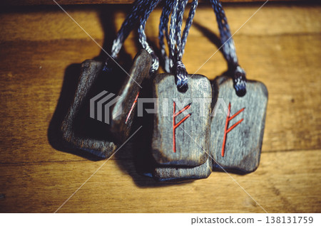 Horizontal group of handcrafted wooden Fehu rune pendants with red carved symbols and dark cords on a rustic wooden surface. Horizontal group of handcrafted wooden Fehu rune pendants with red carved symbols and dark cords on a rustic wooden surface. 138131759