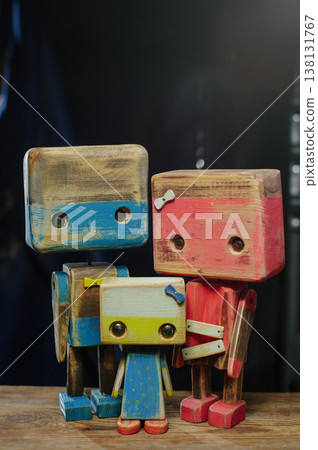 A vertical portrait of a handcrafted wooden robot family, featuring a blue father, red mother, and small yellow child, with distressed textures. A vertical portrait of a handcrafted wooden robot family, featuring a blue father, red mother, and small yellow child, with distressed textures. 138131767