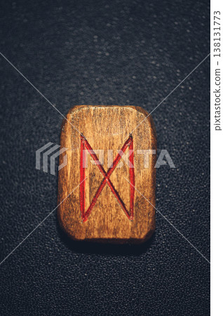 A vertical close-up of a handcrafted wooden Dagaz rune stone, featuring the carved transformation symbol filled with red pigment on a rustic grain. 138131773
