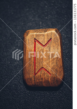 A vertical close-up of a handcrafted wooden Perthro rune stone, featuring the carved symbol filled with red pigment on a rustic grain. A vertical close-up of a handcrafted wooden Perthro rune stone, featuring the carved symbol filled with red pigment on a rustic grain. 138131775